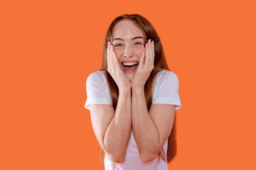 Smiling woman with long hair shows excitement and joy against an orange background during a...