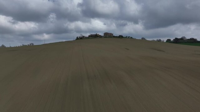 Drone flies over an empty field with a single tree, then ascends toward a hilltop house, revealing a stunning panoramic landscape behind.