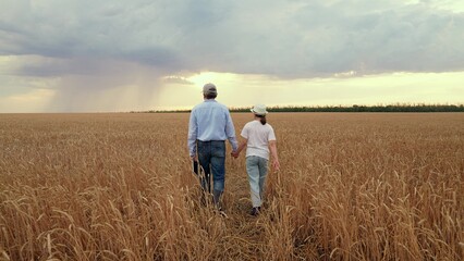 Agriculture father farmer with little daughter working wheat field, child kid baby daughter helping father field. Daughter girl father wheat field. Family business, happy family. Clouds in sky rain