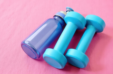Two blue dumbbells and a water bottle lying on a pink yoga mat, top view