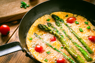 Omelet with tomatoes and asparagus in a pan on a wooden table. Delicious and healthy breakfast.