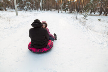 Father and daughter having fun with snow tube in the forest