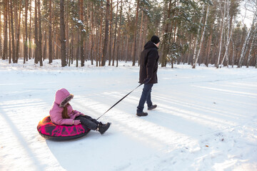 Dad takes his daughter on a snow tube in the forest