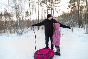 Dad with his daughter walking with snow tubing in the winter forest