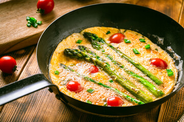 Omelet with tomatoes and asparagus in a pan on a wooden table. Delicious and healthy breakfast.