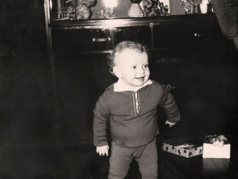 Vintage portrait of a curly little boy. The child is learning to walk. Retro photo from 1967