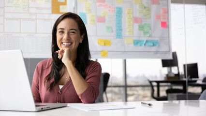 Confident and optimistic. Portrait happy successful young businesswoman scrum master project manager sitting at desk in agile office look at camera laugh at funny moment in work planning. Copy space