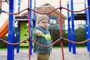 Obraz premium An adorable toddler joyfully playing at an outdoor playground surrounded by a colorful climbing structure and a fun slide, creating a vibrant atmosphere and fostering happy childhood memories