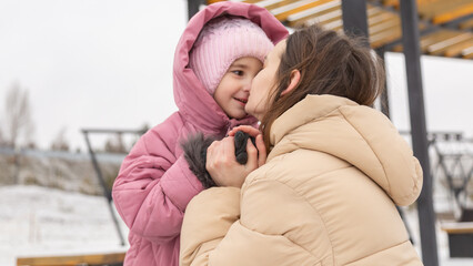 Fototapeta premium Mother and little girl have fun during winter outdoor. Mom playing with kid on fresh frosty air in winter