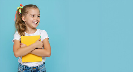 Laughing girl with colorful hair ribbons holding yellow book against bright blue background. Educational portrait for Children's Day, back to school campaigns and literacy promotion events
