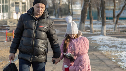Grandfather walks with his granddaughters after school in the park in sunny winter day