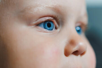 This is a closeup portrait photograph of an infants face, capturing their sparkling blue eyes and the incredibly soft and delicate textures of their skin, radiating beauty and innocence