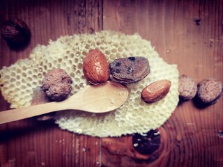 Honey in honeycomb with wooden spoon, almonds and walnuts in shell