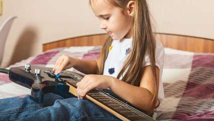 Little girl learning to play guitar at home. Selective focus