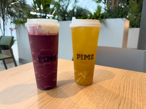 Moscow, Russia, April 25, 2025: Two signature drinks from PIMS cafe served on wooden table. Bright colors, layered textures and fresh ingredients highlight modern bubble tea presentation