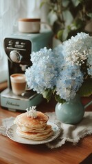 A stack of pancakes, coffee machine, and hydrangea flowers.  A cozy breakfast scene
