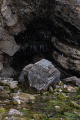 Cave with a stream flowing out and a mossy rock