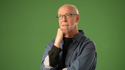 A senior man stands confidently against a solid green backdrop, showing joy with a bright smile and relaxed demeanor, captured during a portrait session.