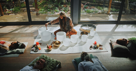 Woman, singing bowl and group on floor for sound, therapy or lying with mindfulness at studio. Person, homeopath and guide at class with crystal, above and zen for chakra balance for holistic healing