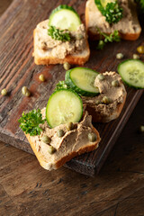  Open sandwiches with pate, cucumber, capers, and parsley on a old cutting board.