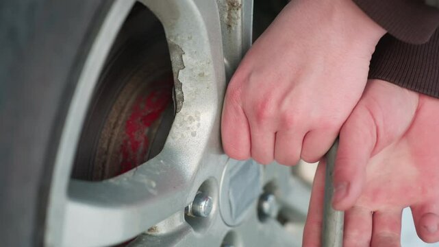 Close-up of person hand using spanner to loosen bolt on car rim, focus on tool action with clear details of wheel and metal surface, preparing for tire change or repair in outdoor environment