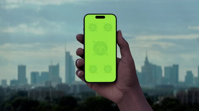 GREEN SCREEN CHROMA KEY Hand holding a phone with a city skyline in the background. Ideal for mockups of taxi, betting, or travel apps set in an urban environment