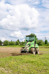 Mini skid steer loader clear a construction site. Small tractor with a ground leveler moves soil. Land work by the territory improvement, plot leveling. Plowing agricultural field. High quality photo.
