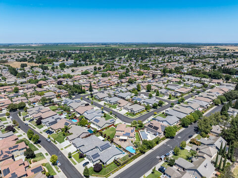 Aerial view of a suburban residential neighborhood in Stockton, California, showcasing rows of single-family homes, streets, and surrounding farmland. Ideal for topics related to urban planning, Calif