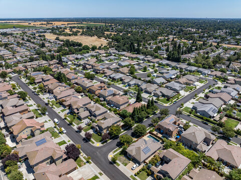 Aerial view of a suburban residential neighborhood in Stockton, California, showcasing rows of single-family homes, streets, and surrounding farmland. Ideal for topics related to urban planning, Calif