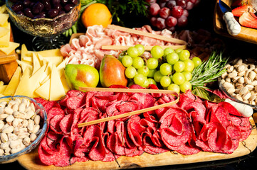 table of cold cuts, nuts, fruits, and cheeses at a food station at a party
