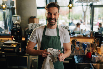 Smiling barista polishing glass in coffee shop