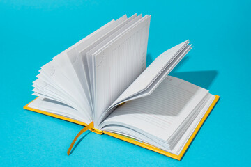 Photo of opened notebook on turquoise blue background with copy space. Minimalist image of blank diary in perspective. Stylish shot of a notebook with harsh light and shadow.