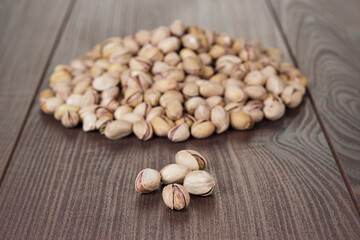 Many roasted pistachios on the wooden table. Close-up photo of some pistachios and a pile of pistachios in background.