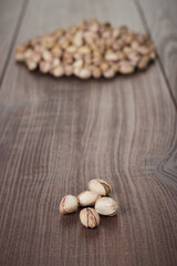 Close-up photo of some pistachios and a pile of pistachios in background. Many roasted pistachios on the wooden table.