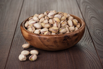 Wooden bowl full of roasted pistachios on the wooden table.