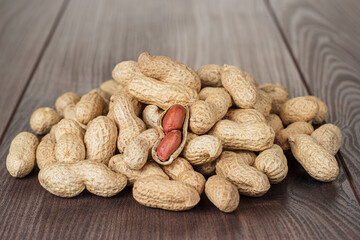 Many roasted peanuts on the wooden table. Pile of unshelled peanuts and a shelled one in the centre.