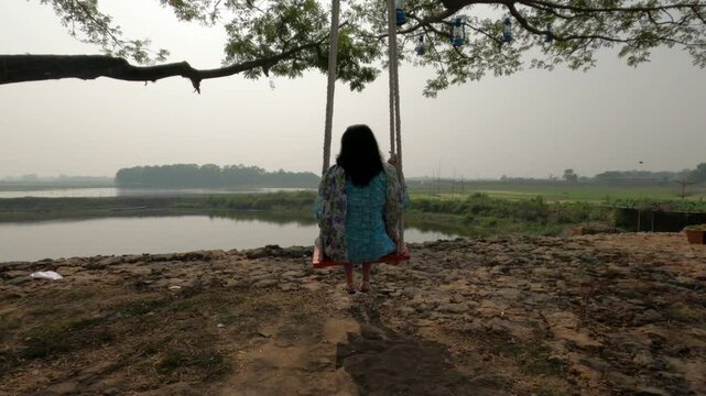 A woman wearing salwar kameez and and swinging on rope in front of pond in Dhaka, Bangladesh