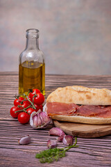 Sliced ​​bread, garlic cloves, seasonings, cherry tomatoes, olive oil, and Serrano ham to make a typical Spanish sandwich