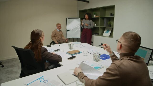 Black female office manager presenting at whiteboard with partner in wheelchair answering colleagues question during board meeting while interacting with audience of coworkers in conference room