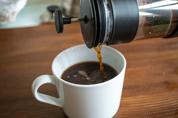 Brewing and pouring coffee with black french press on table in close-up