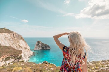 A woman stands at the edge of a cliff in Zakynthos, Greece, gazing towards the picturesque bay and...