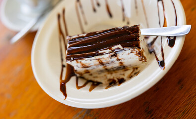 On plate is slice of creamy ice cream, sprinkled with chocolate chips and decorated with whipped cream. Treat from chef for visitors of coffee shop.
