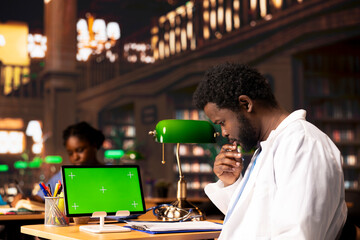 Medical student uses books in the campus study space next to green screen, combining research, anatomy lessons and academic methods. Pupil reading research papers for medical practice.