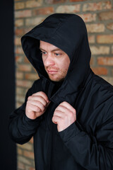 A young man dressed in a stylish black hooded jacket is posing confidently against a rustic brick wall. This image beautifully captures the essence of fashion and urban style photography