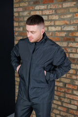 A Stylish Young Man Dressed in Trendy Casual Outdoor Clothing, Posing Confidently Against a Textured Brick Wall, Emanating A Cool Lifestyle and Fashion Sense That Captures Attention