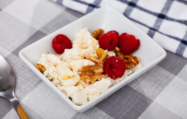 Fresh farm cottage cheese filled with large amount of liquid summer honey is served on plate, decorated with walnut and raspberry