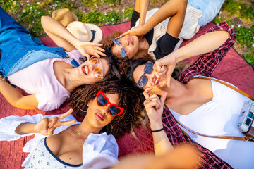 Four young women lying on blanket taking selfie in park