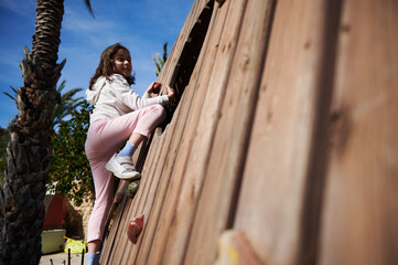 Young Girl Climbing an Outdoor Wooden Wall on a Sunny Day