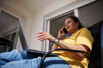 Woman in a Yellow Shirt Using a Laptop and Phone Outdoors