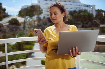 Female Professional Using Smartphone and Laptop on Balcony with Scenic View